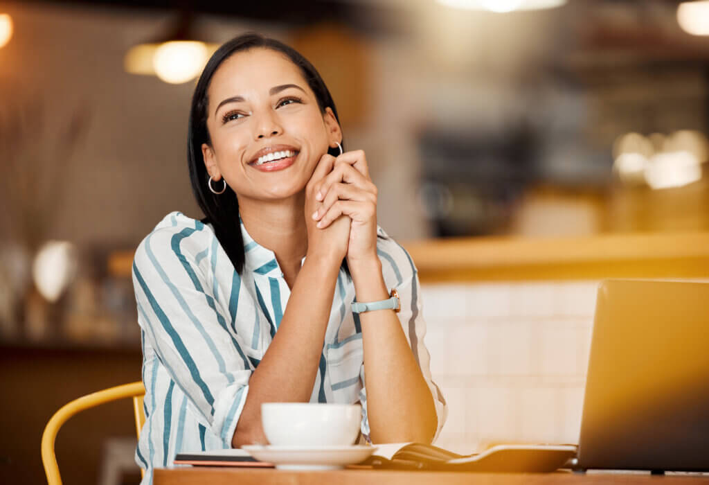 Thinking, smiling and happy young woman in a coffee shop