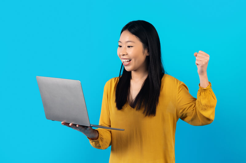 Thrilled happy young asian woman in casual outfit holding modern pc laptop, looking at pc screen, smiling and gesturing