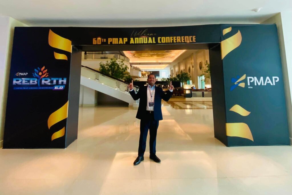 man in suit standing in front of PMAP conference sign