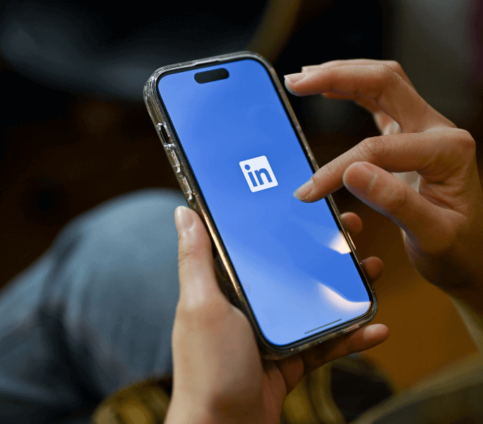 person holding mobile phone with the screen showing LinkedIn logo; optimize your LinkedIn profile concept