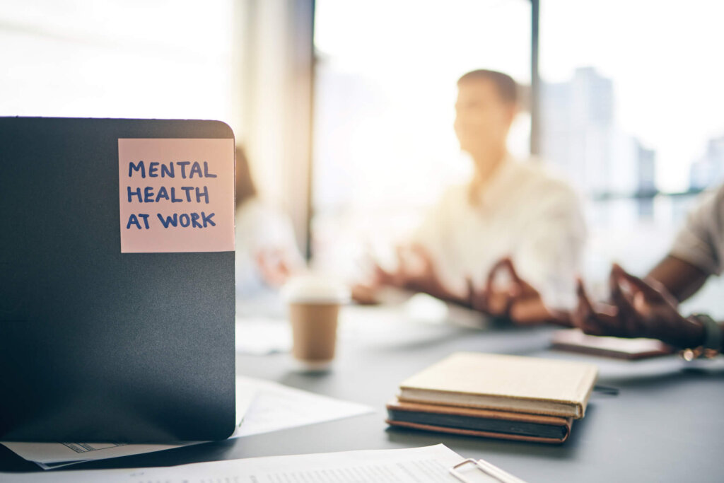 mental health at work written on a post-it in the foreground and employees meditating in the background